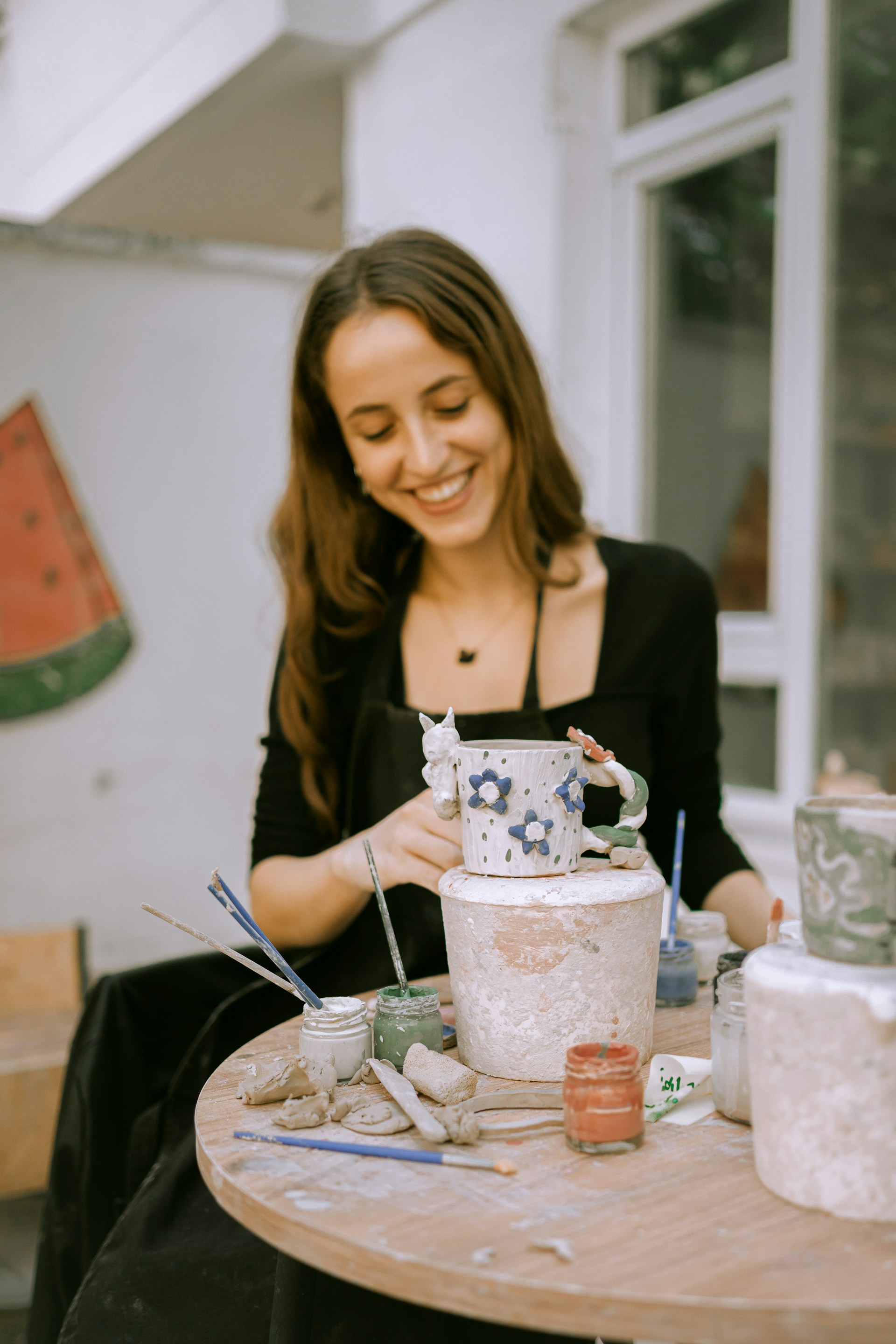 A studio guest smiling while hand-painting a ceramic mug at Potters Clay